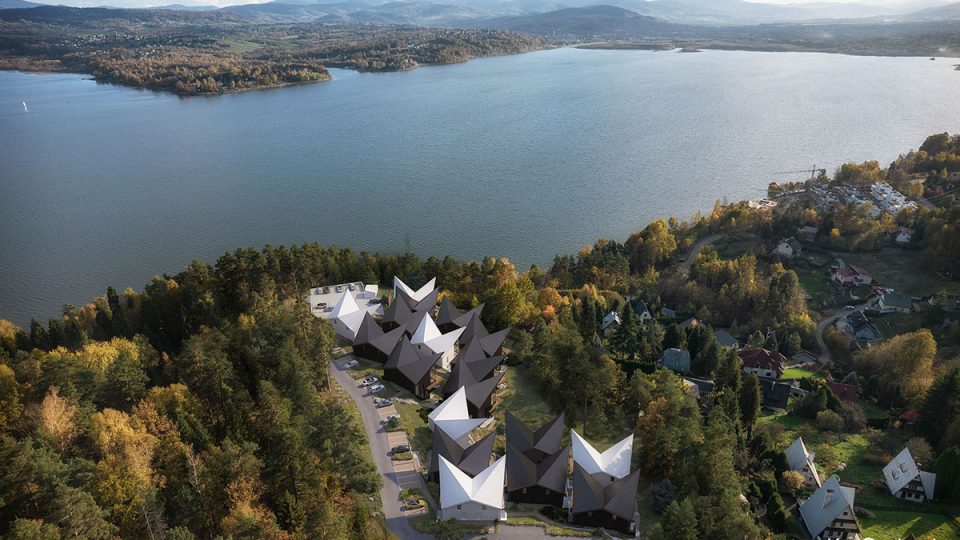 A bird’s-eye view visualization showcasing a residential estate of modern luxury mountain villas situated on a slope with a lake view.